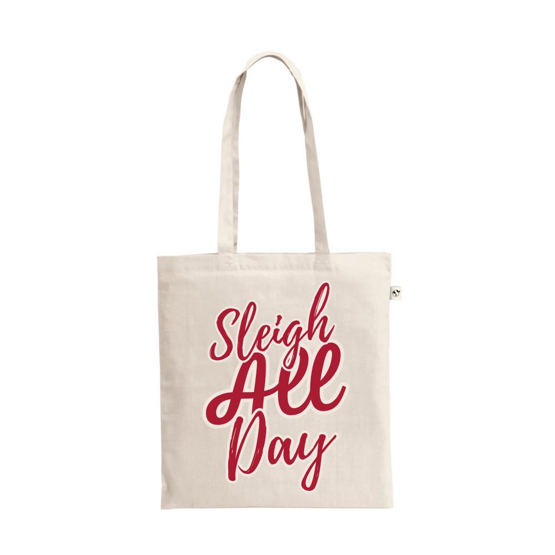 A natural cotton tote bag featuring the playful text "Sleigh All Day" in a bold, cursive, red script.